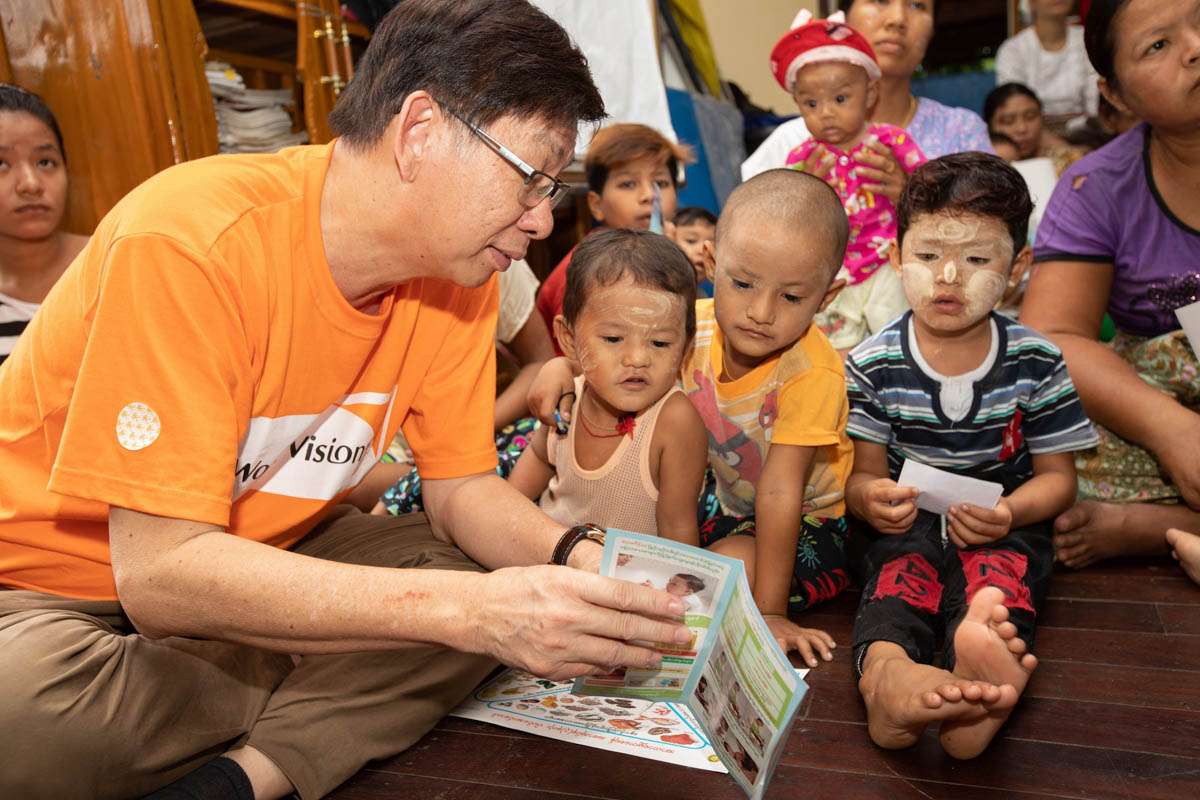 Photo-1-Boey-reads-a-pamphlet-on-proper-handwashing-techniques-to-a-few-preschool-children-in-Myanmar.jpg